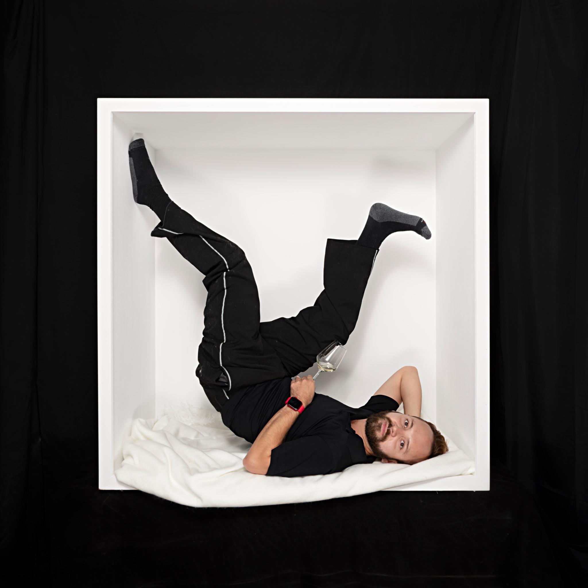 A sitter in black reclines upside down in the white box, with both legs raised into the air.