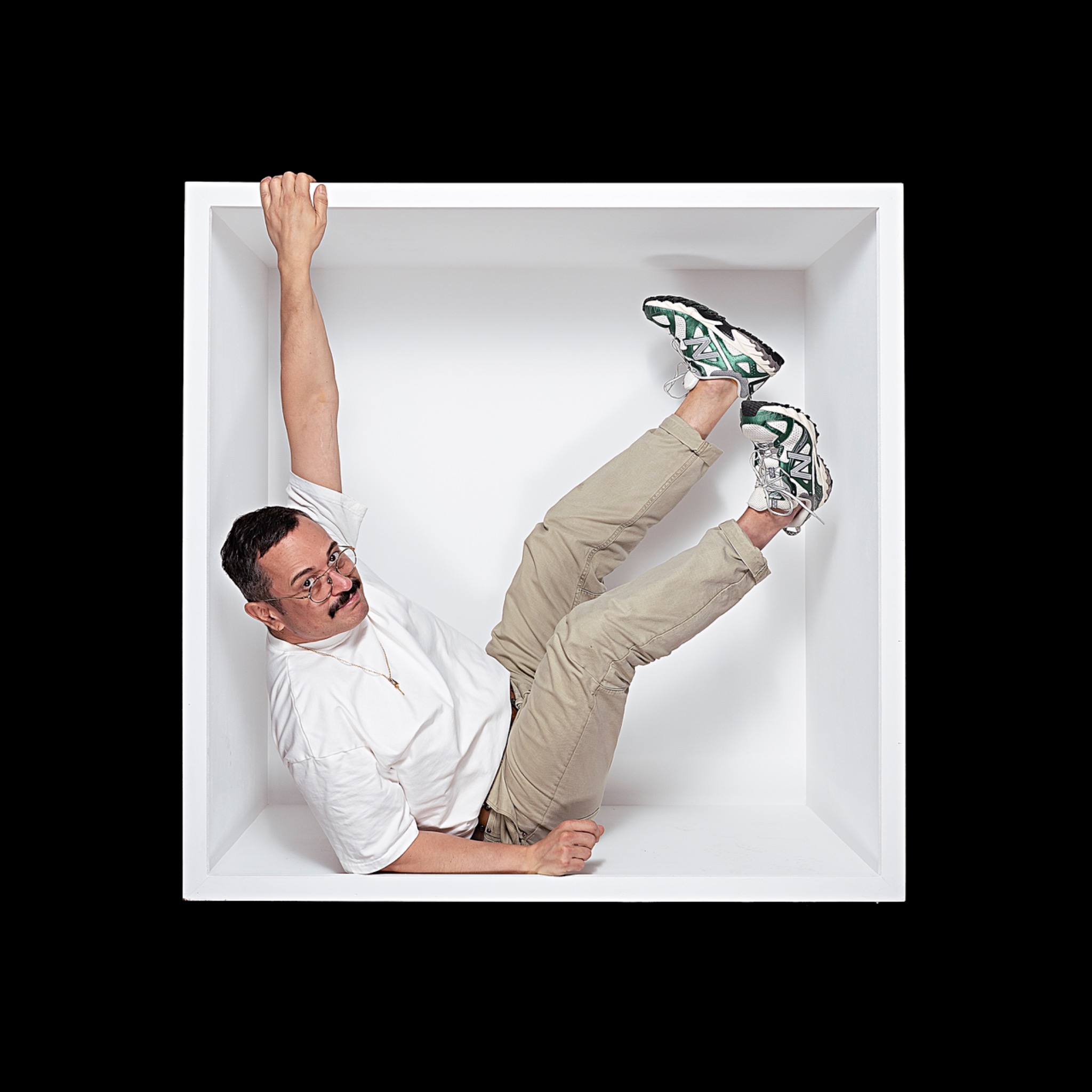 A sitter in a white shirt and beige trousers holds the top edge of the box, with patterned trainers raised diagonally.