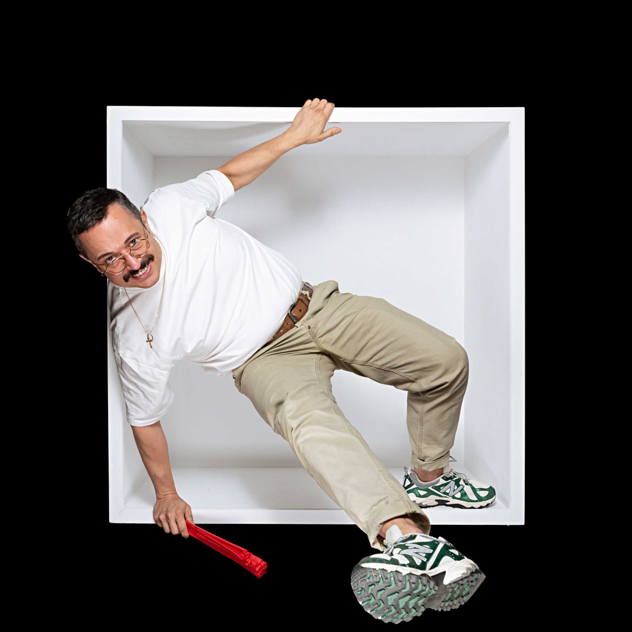 A smiling sitter steps out of the white box, bringing a patterned trainer forward and holding a red fan.