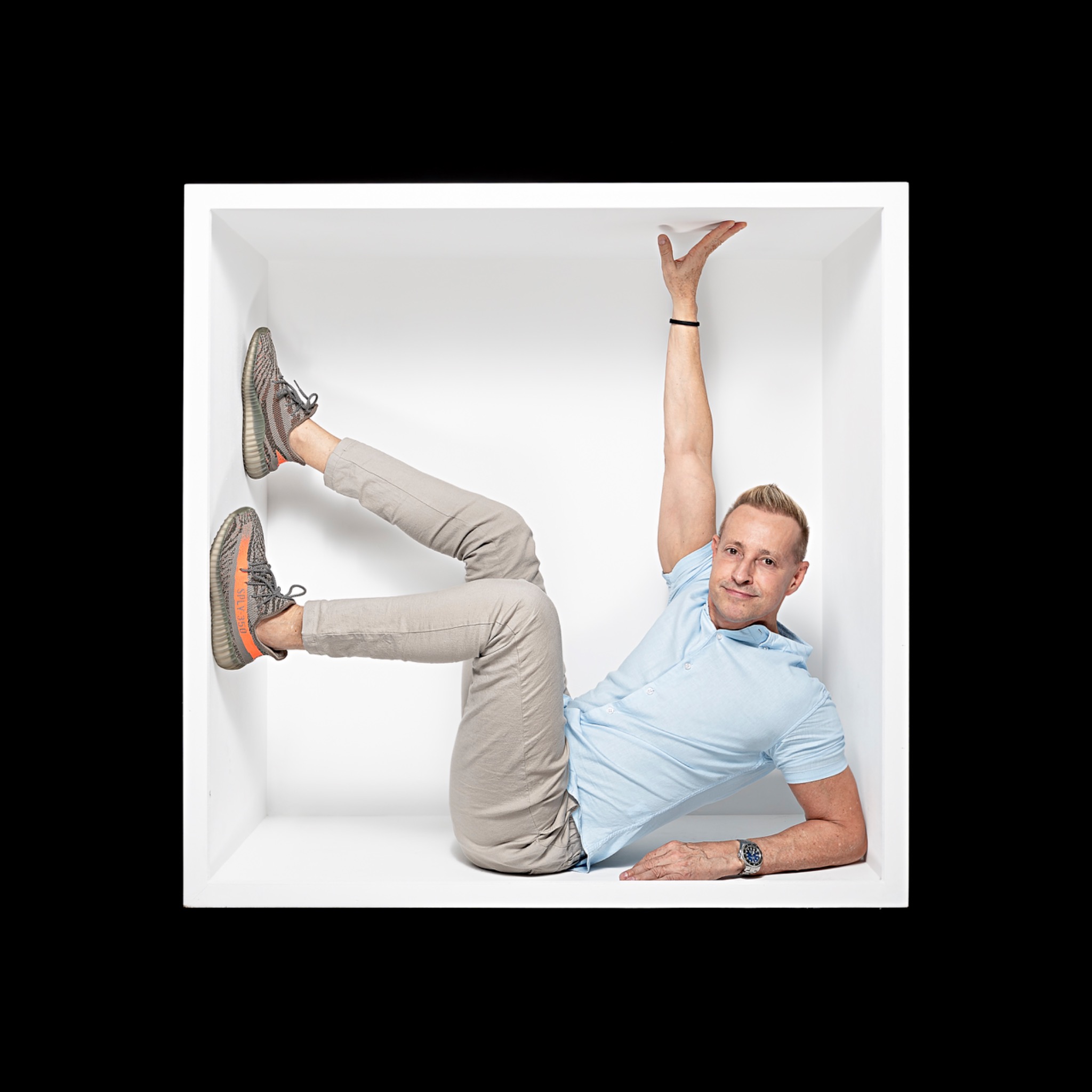 A sitter in a pale blue shirt reclines diagonally in the white box, with one arm reaching up and both legs raised.