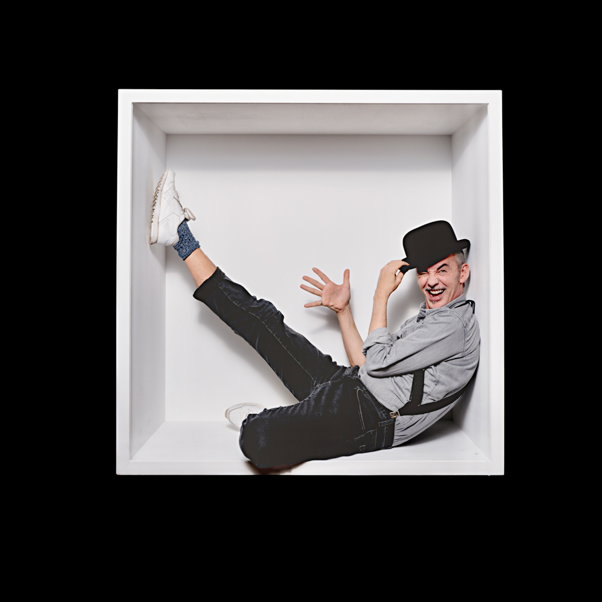 The grey-haired sitter smiles beneath a black top hat, with one leg raised against the side of the white box.