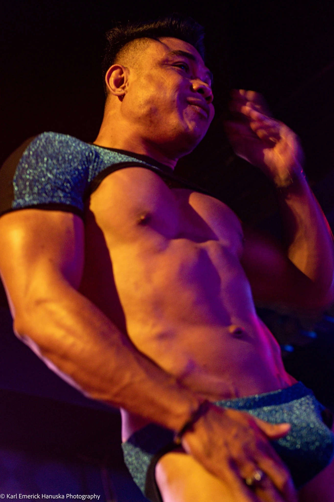 A dancer in blue briefs moves under amber and violet lighting.