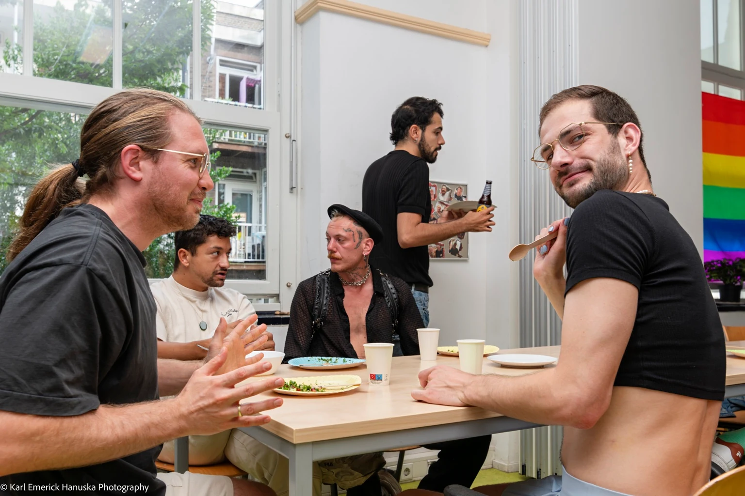 Guests talk across a dining table while a person in glasses turns towards the camera.