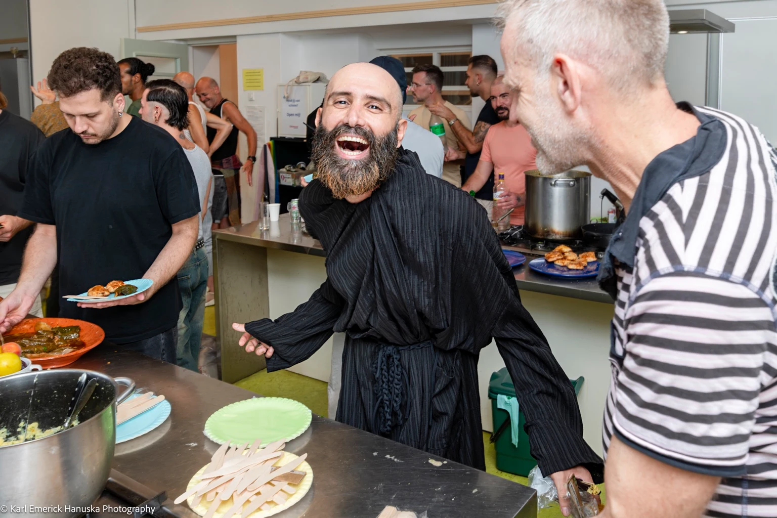 A person in flowing black clothing laughs beside the serving counter as guests collect food.