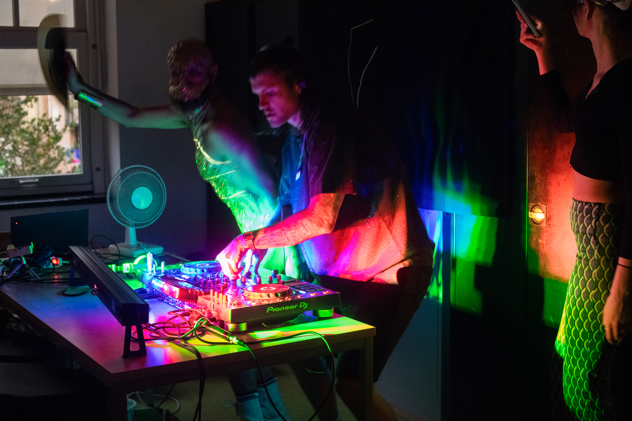 A DJ and dancers appear in saturated coloured light.