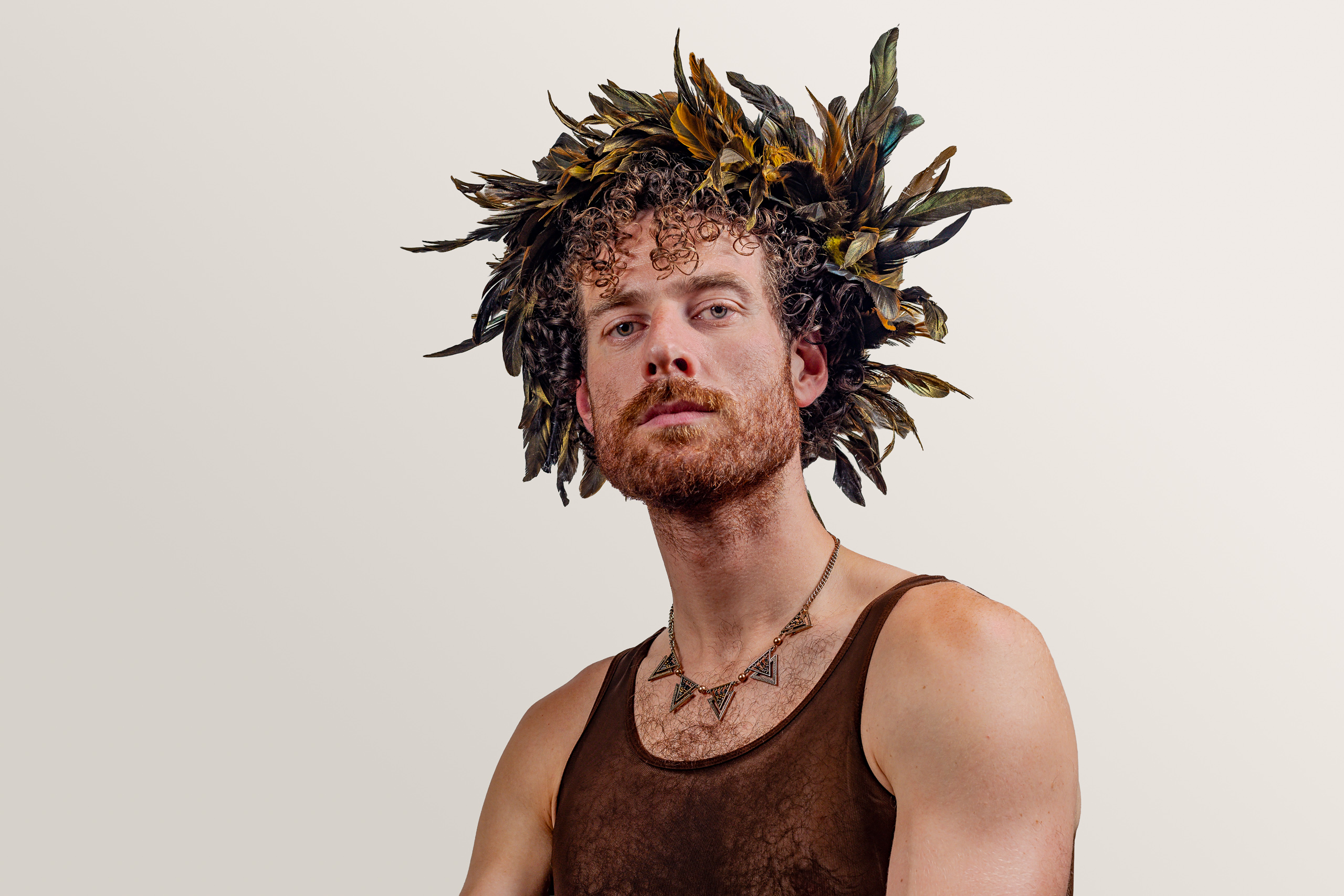 A sitter with curly hair wears a feathered headpiece and a brown mesh top.