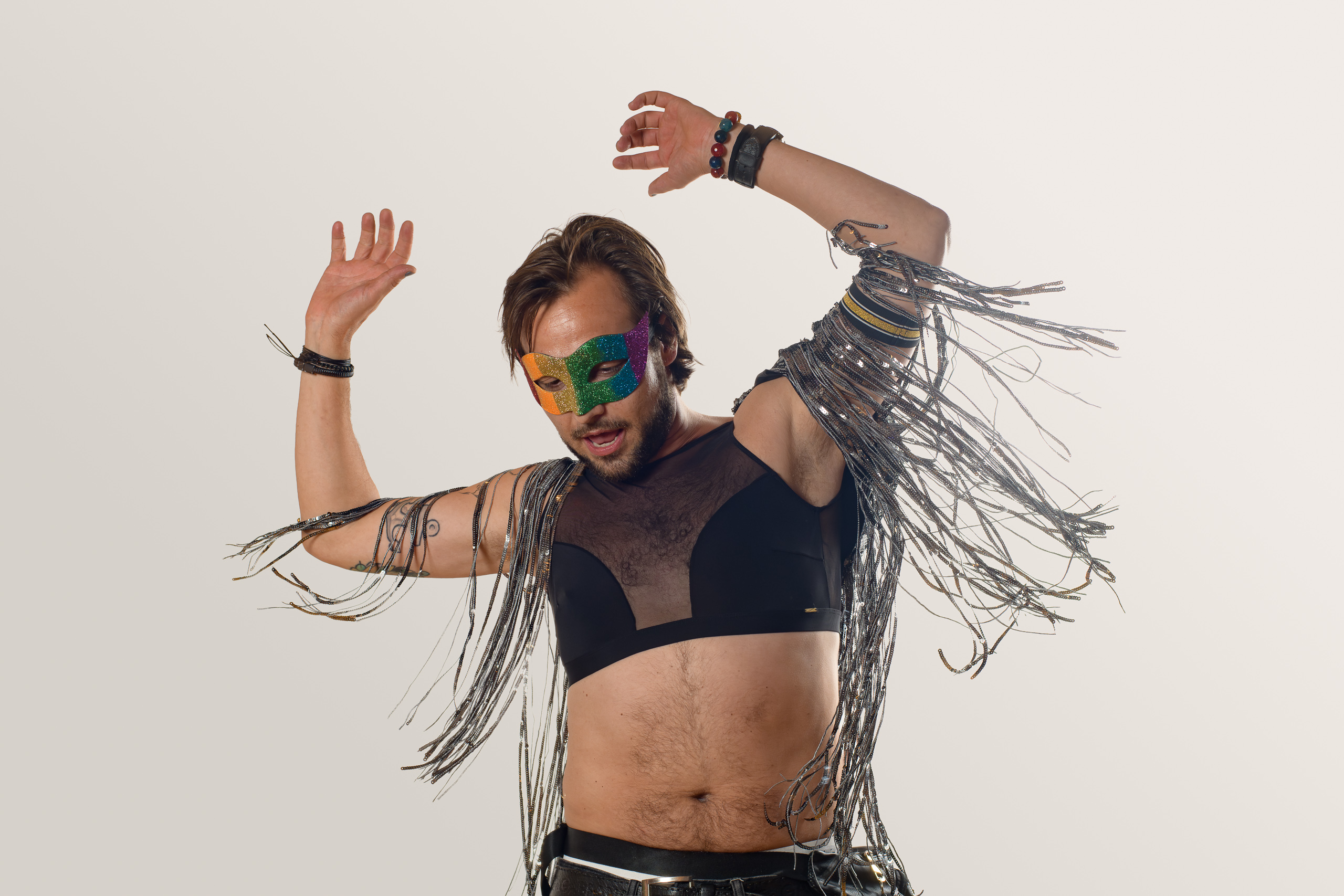A performer in silver fringe and a colourful mask raises both arms in motion.