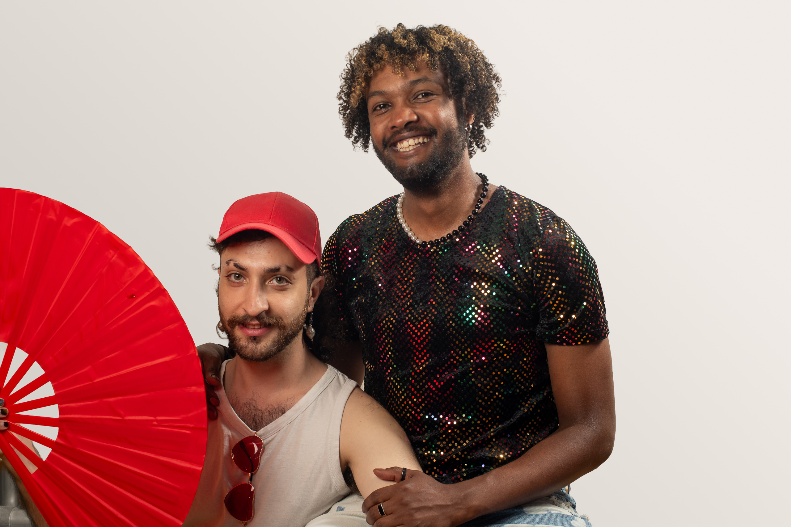 Two smiling people pose together beside a large red fan, one wearing a red cap.
