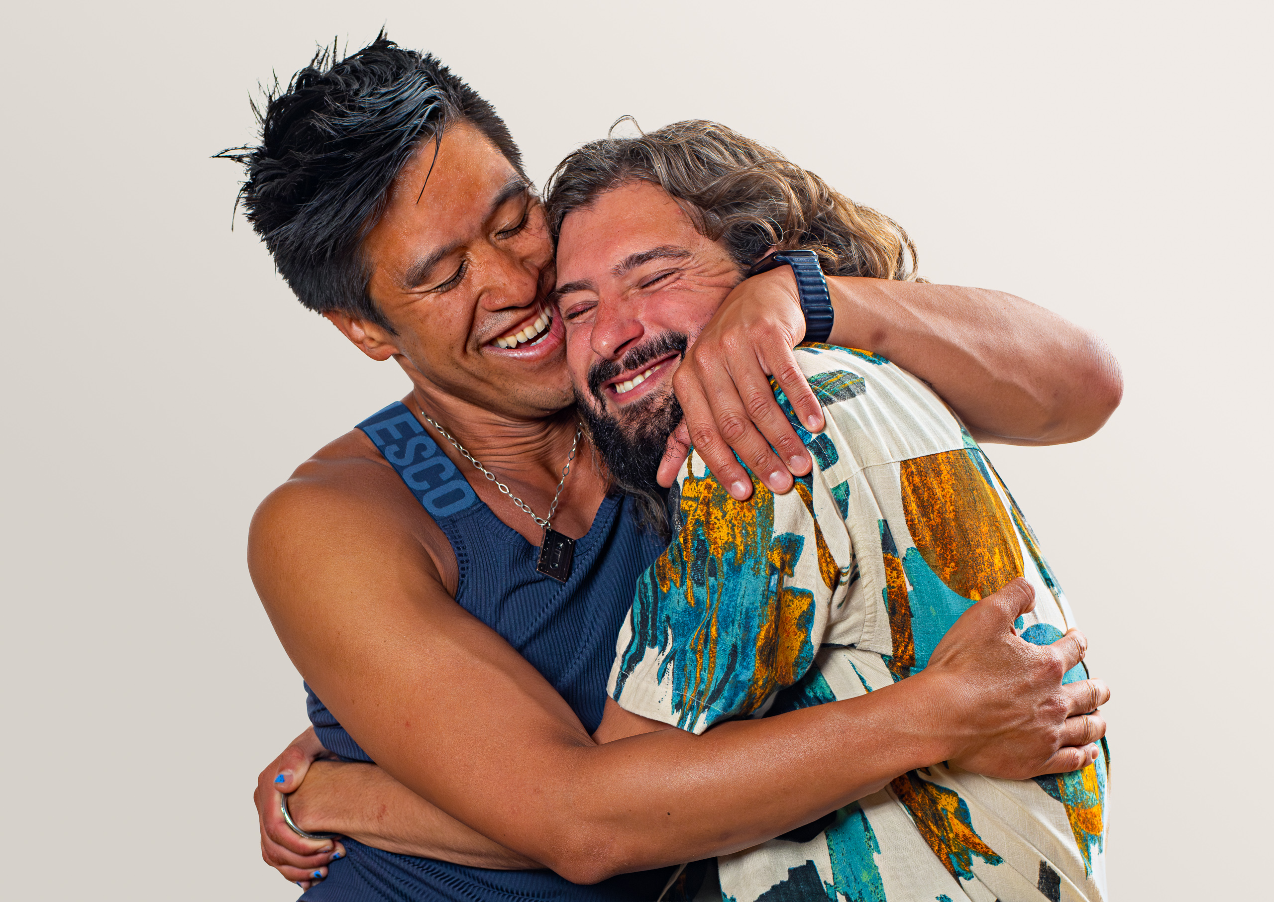 Two people laugh in a close embrace, wearing blue and a colourful patterned shirt.