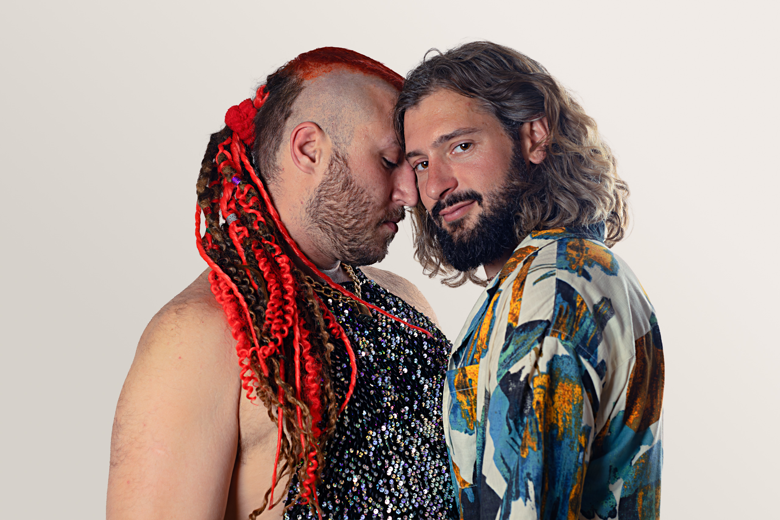Two people lean their heads together, one with red braids and the other in a patterned shirt.