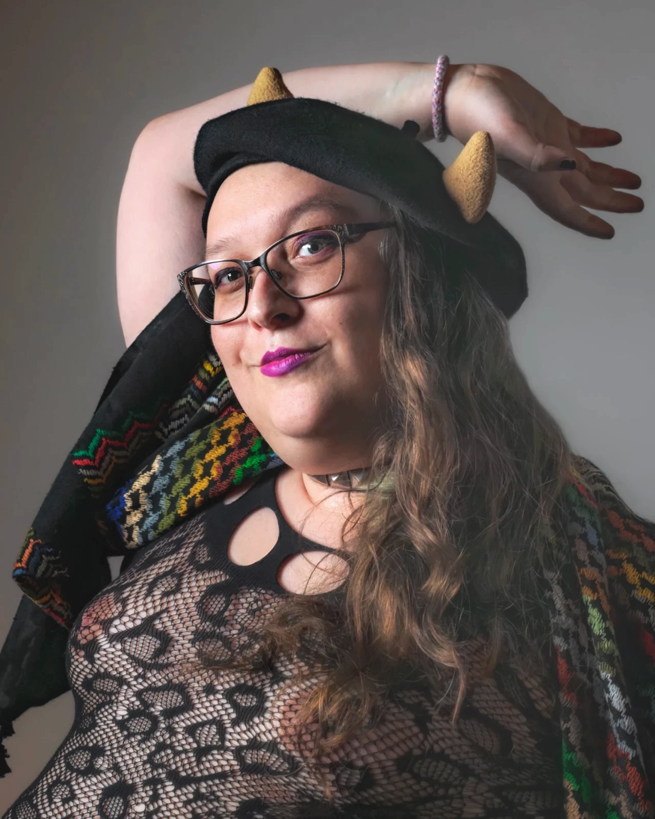 A sitter in glasses, a horned beret and a lace top curves one arm above the head.