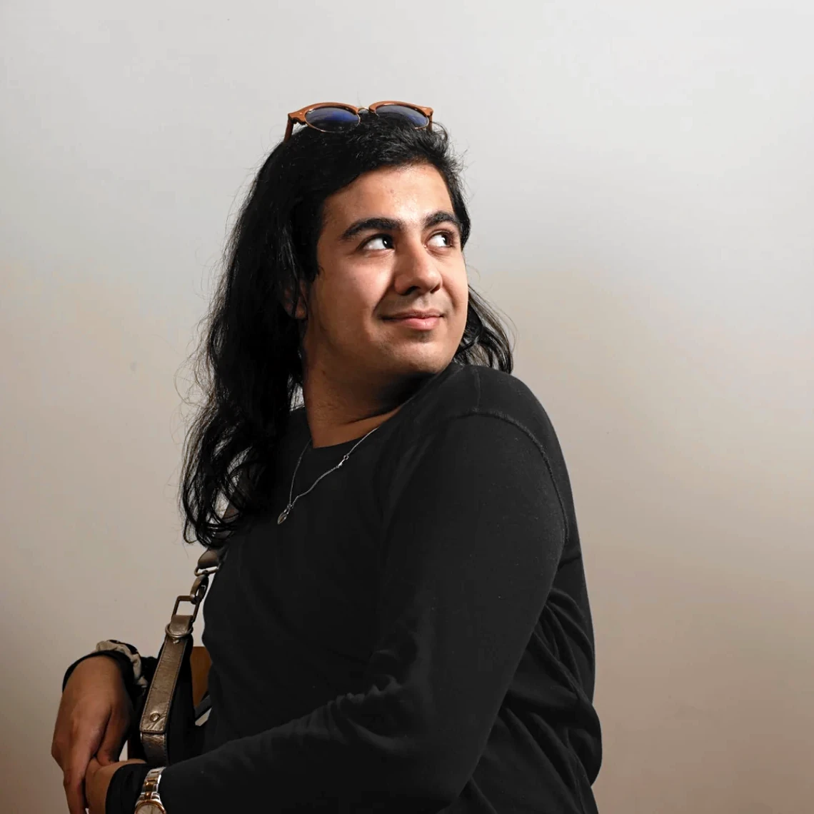 A seated person in black looks sideways, with sunglasses resting on the head and open space around the figure.