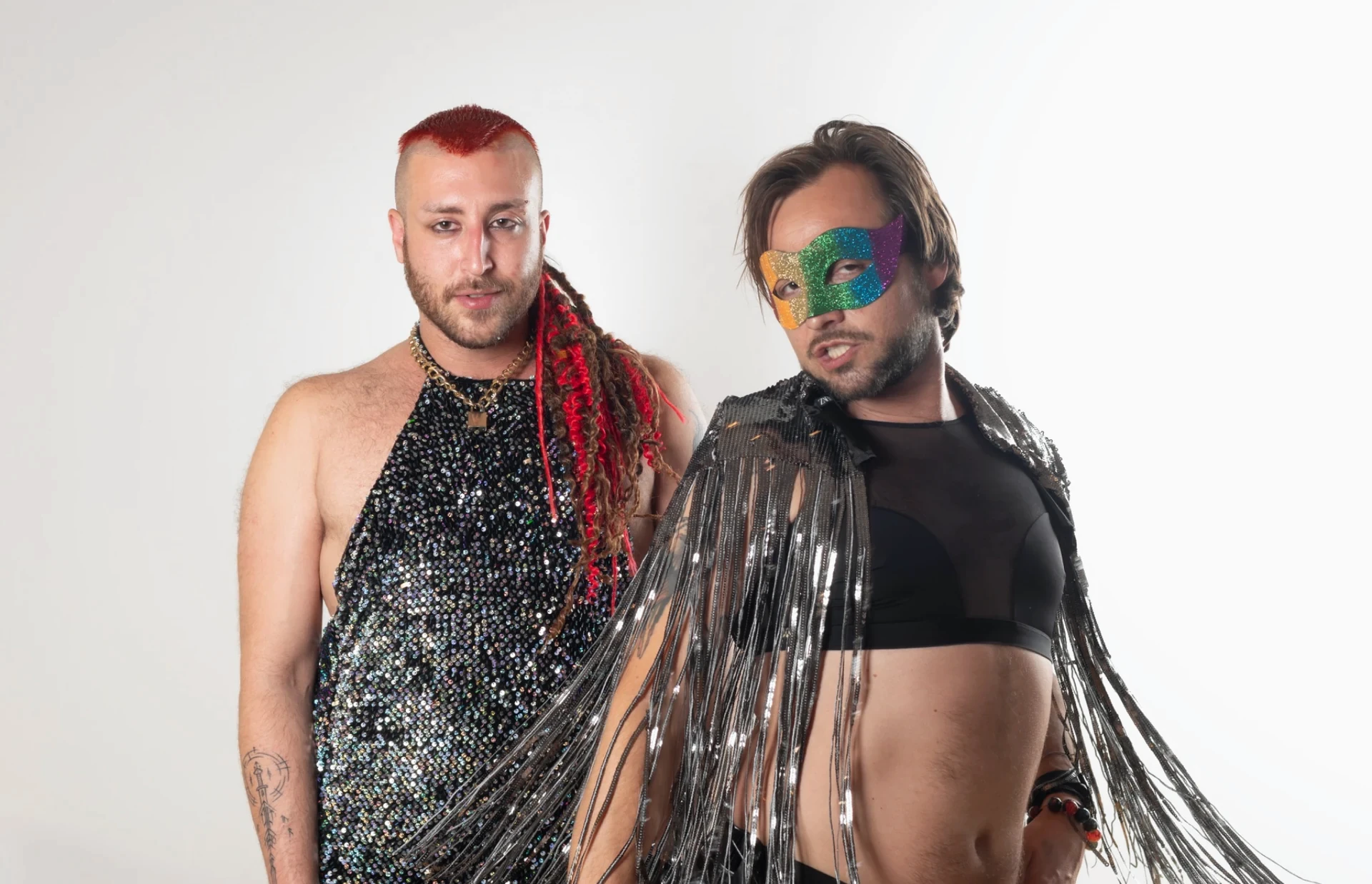 Two sitters stand close together in silver sequins and fringe, one wearing a rainbow mask and the other with long red braids.