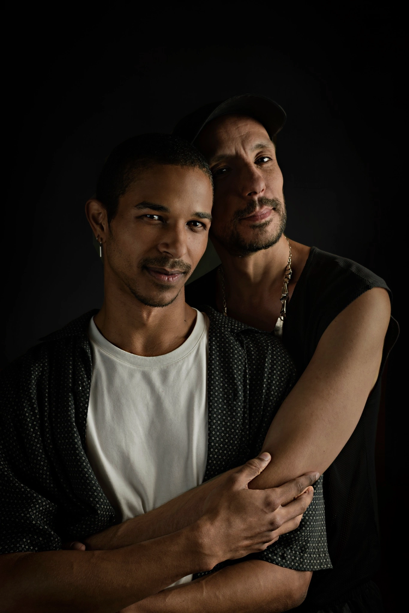 Two sitters hold one another in an intimate portrait against a dark background.