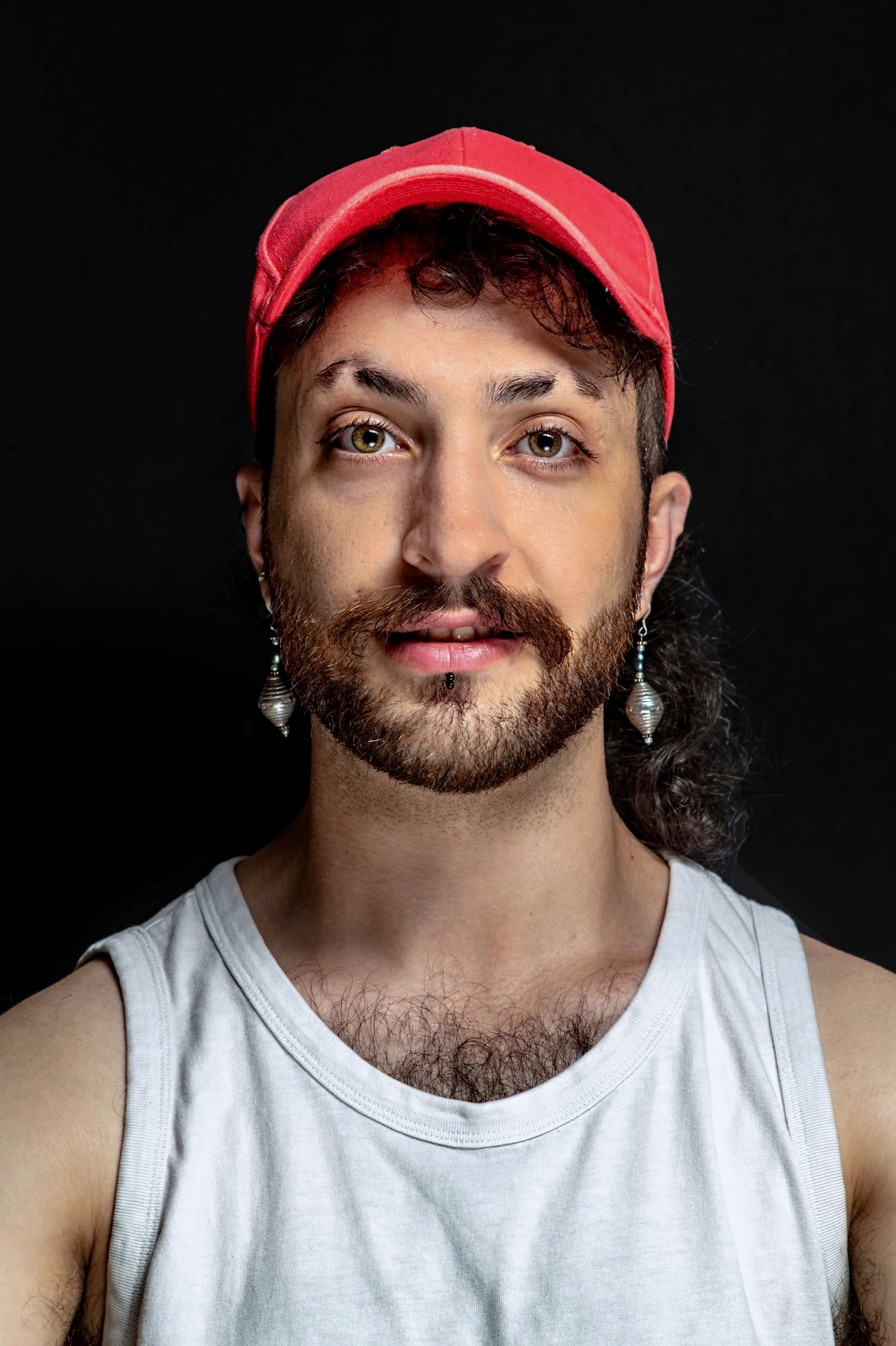 A sitter in a red cap, long earrings and a white tank top looks upward.