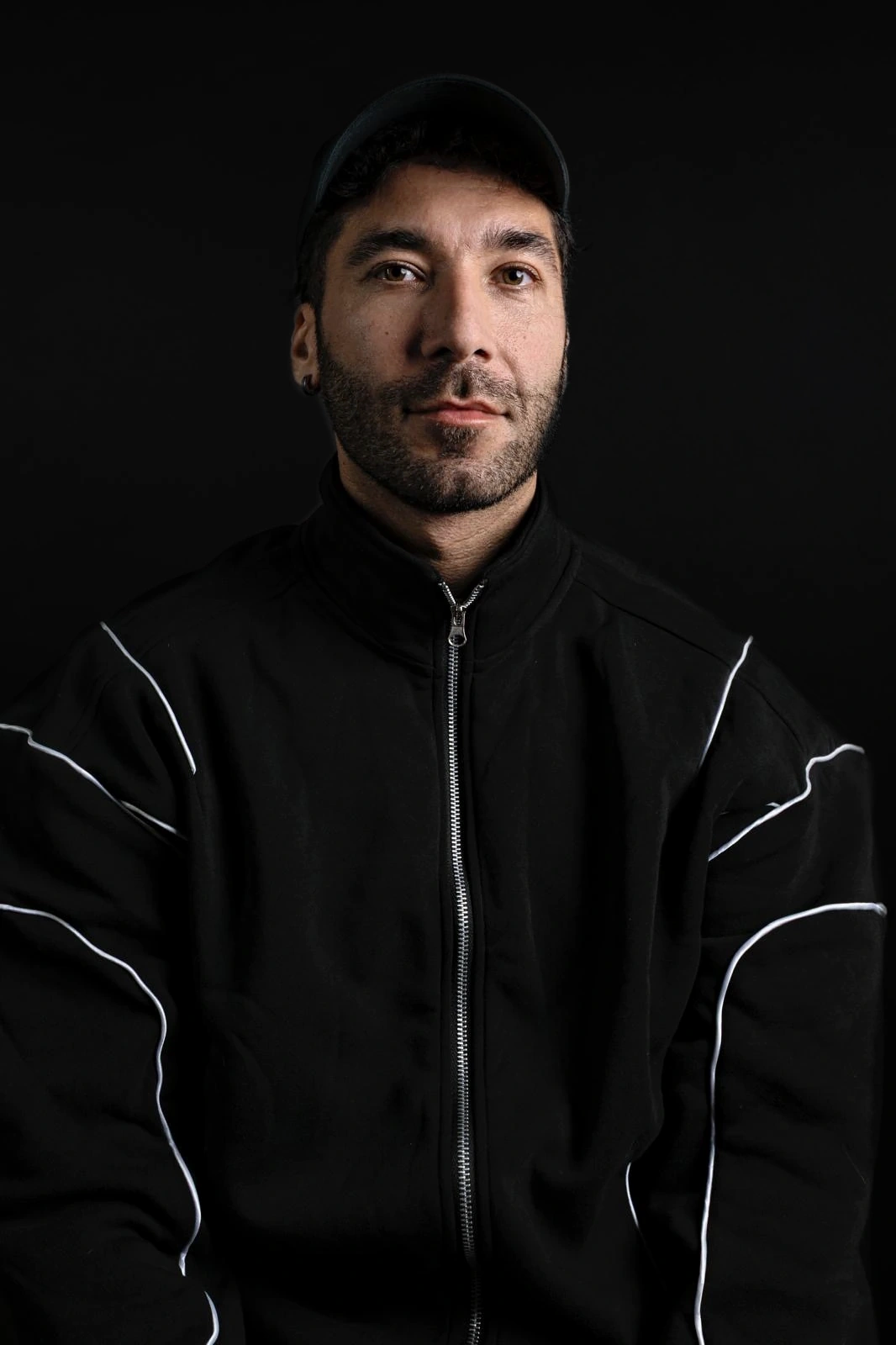 A sitter in a black cap and zip-up jacket with white piping looks directly into the camera.