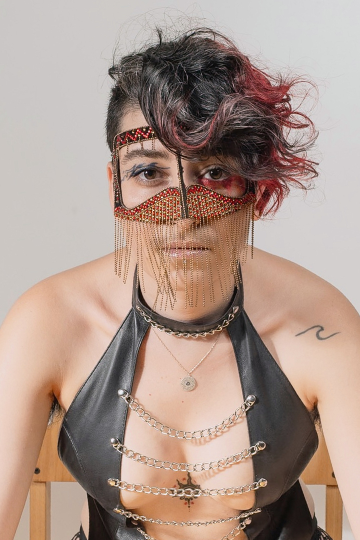 A centred close portrait of Niloo wearing a decorative mask with fine gold chains.