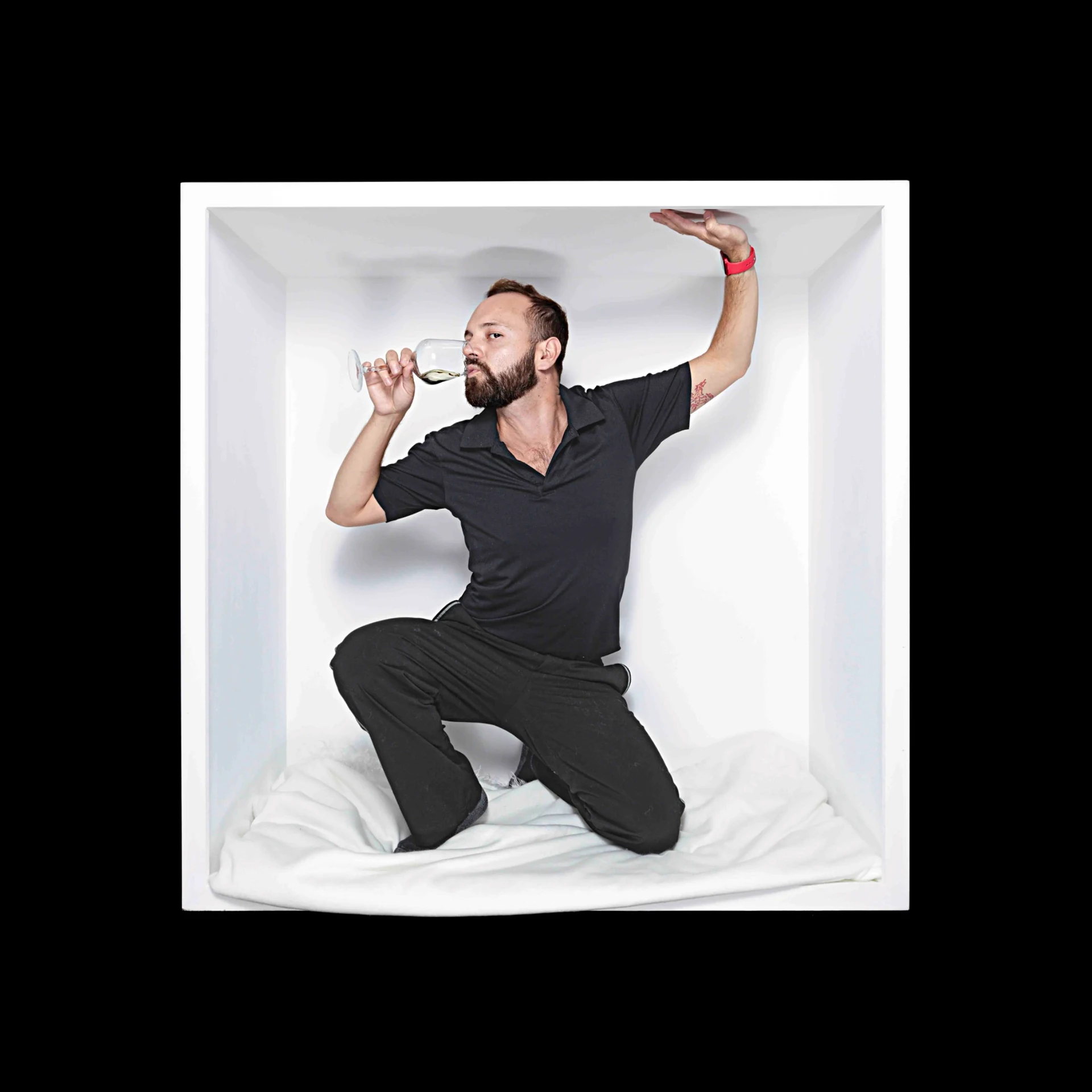 A sitter kneels inside a white box, holding a wine glass and reaching toward its ceiling.