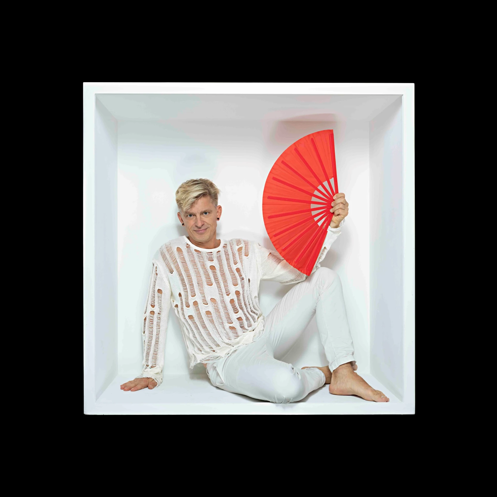 A sitter in a pale striped top sits inside a white box holding a red fan.