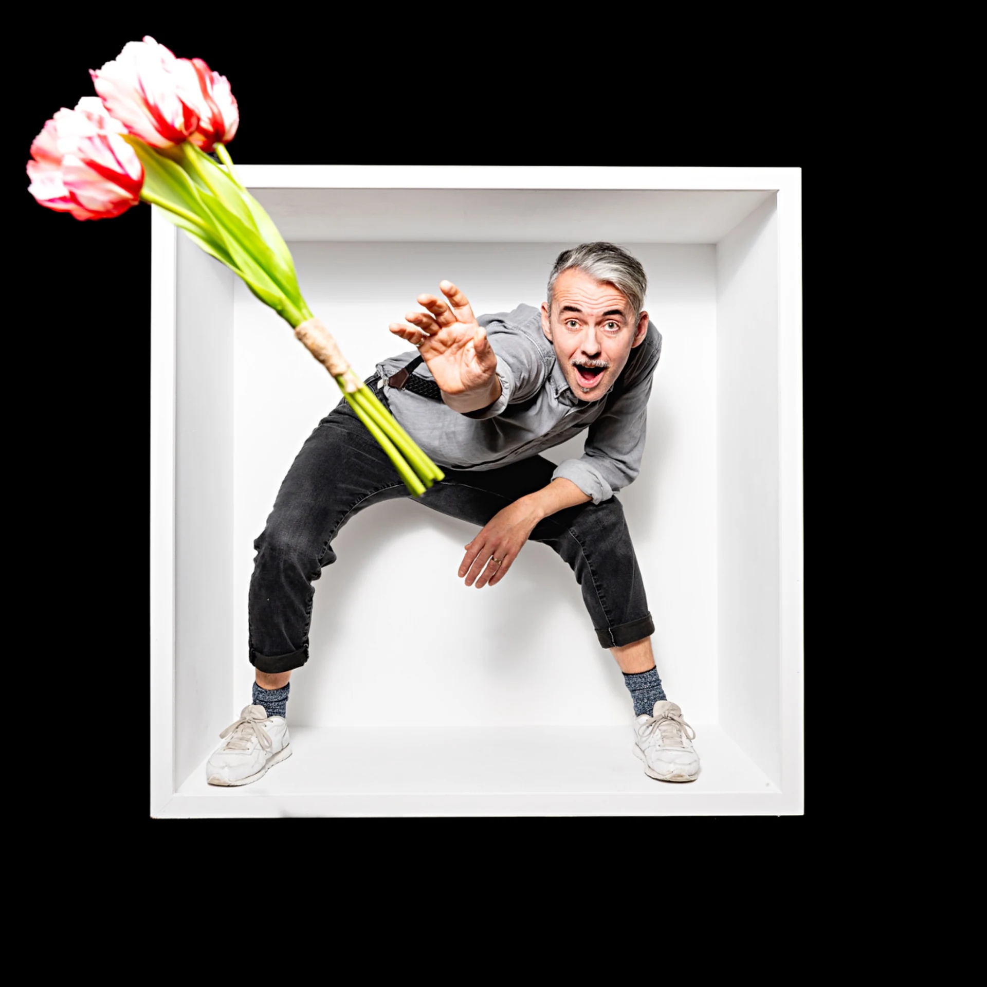 A sitter in a grey shirt reaches toward flowers inside a white box.