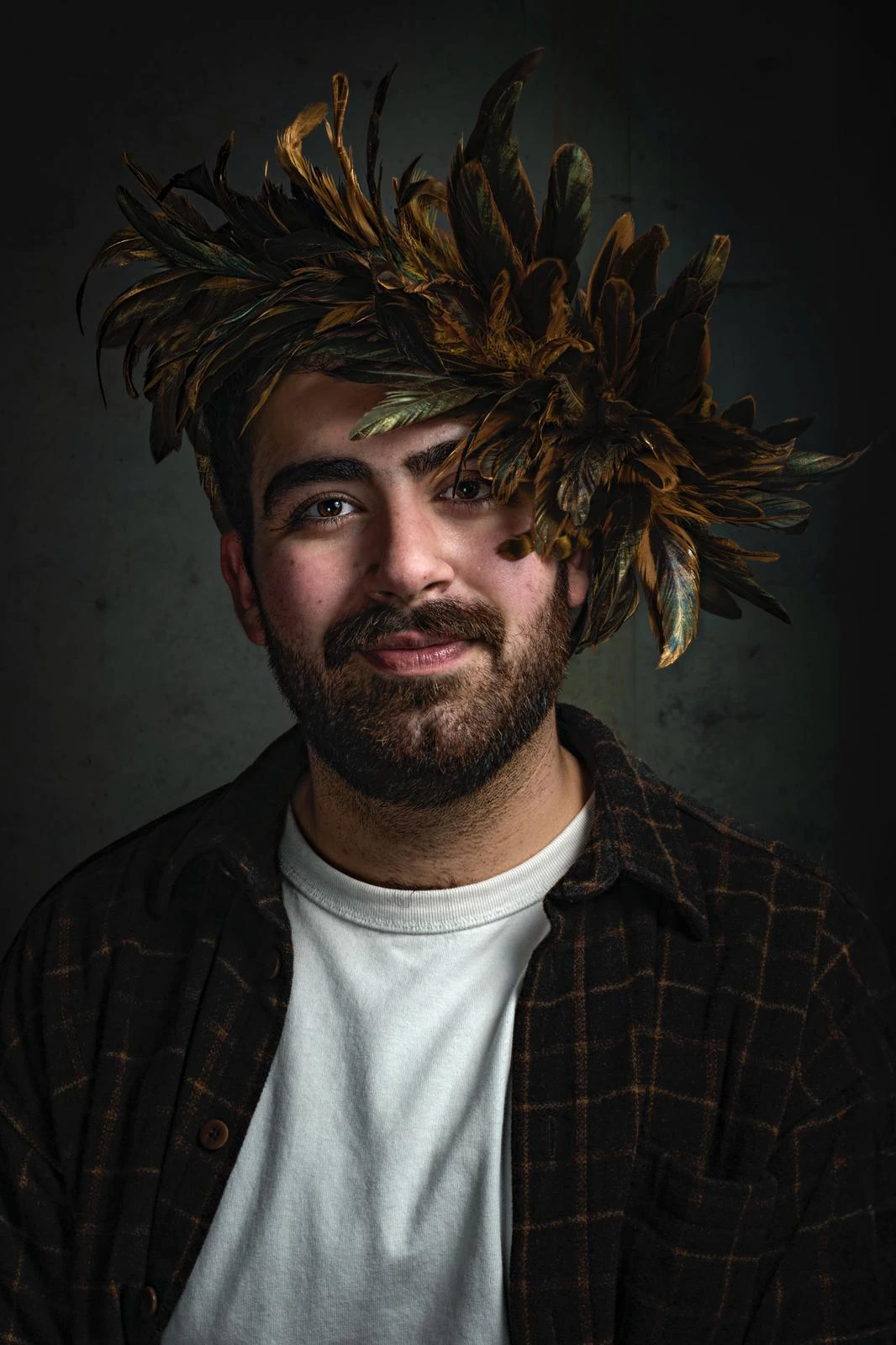 A bearded sitter in a checked overshirt wears the golden feather headpiece, its feathers fanning around the face.