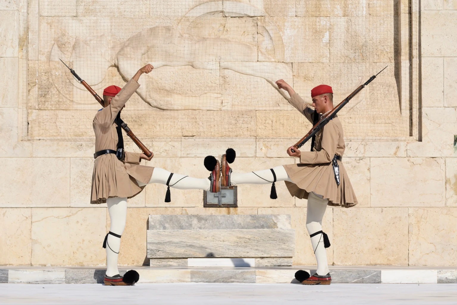 Two guards face one another with raised legs and arms, their mirrored movements framed by a carved stone relief.