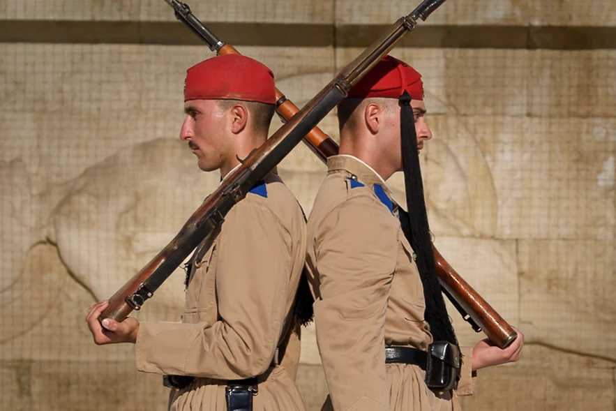 Two guards stand back to back, their tan uniforms and crossing rifles forming a mirrored composition.