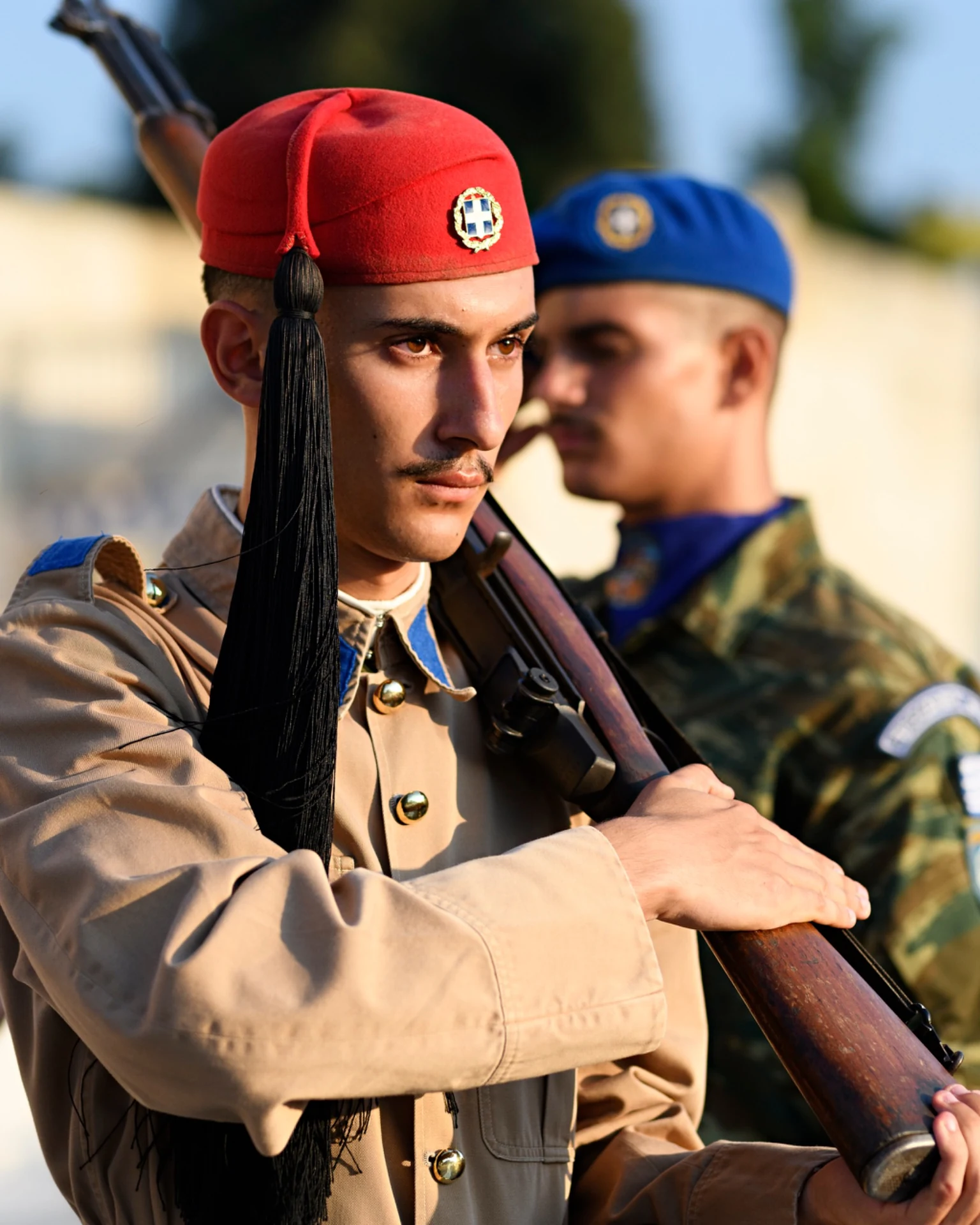 A guard holding a rifle is in focus in front of another guard in a blue beret.