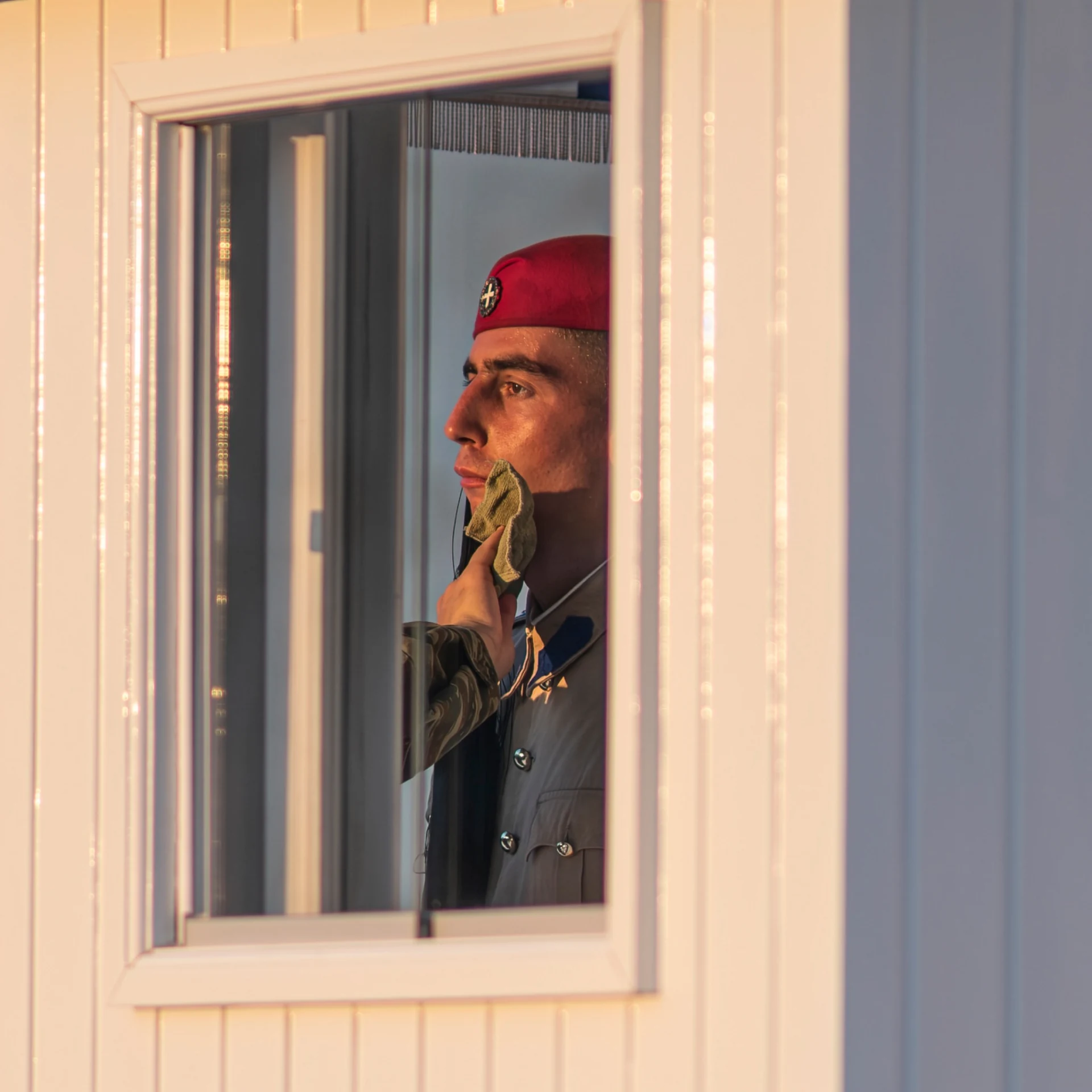 A guard in profile looks through a sentry-box window lit by warm, low sunlight.