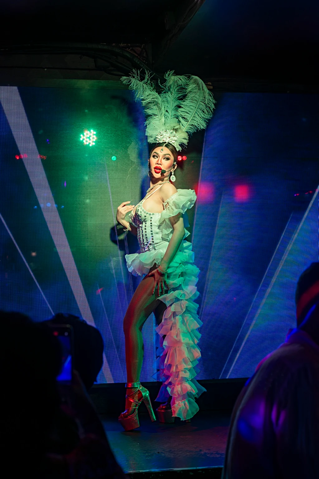 A performer in a white feather headdress and ruffled costume on stage.