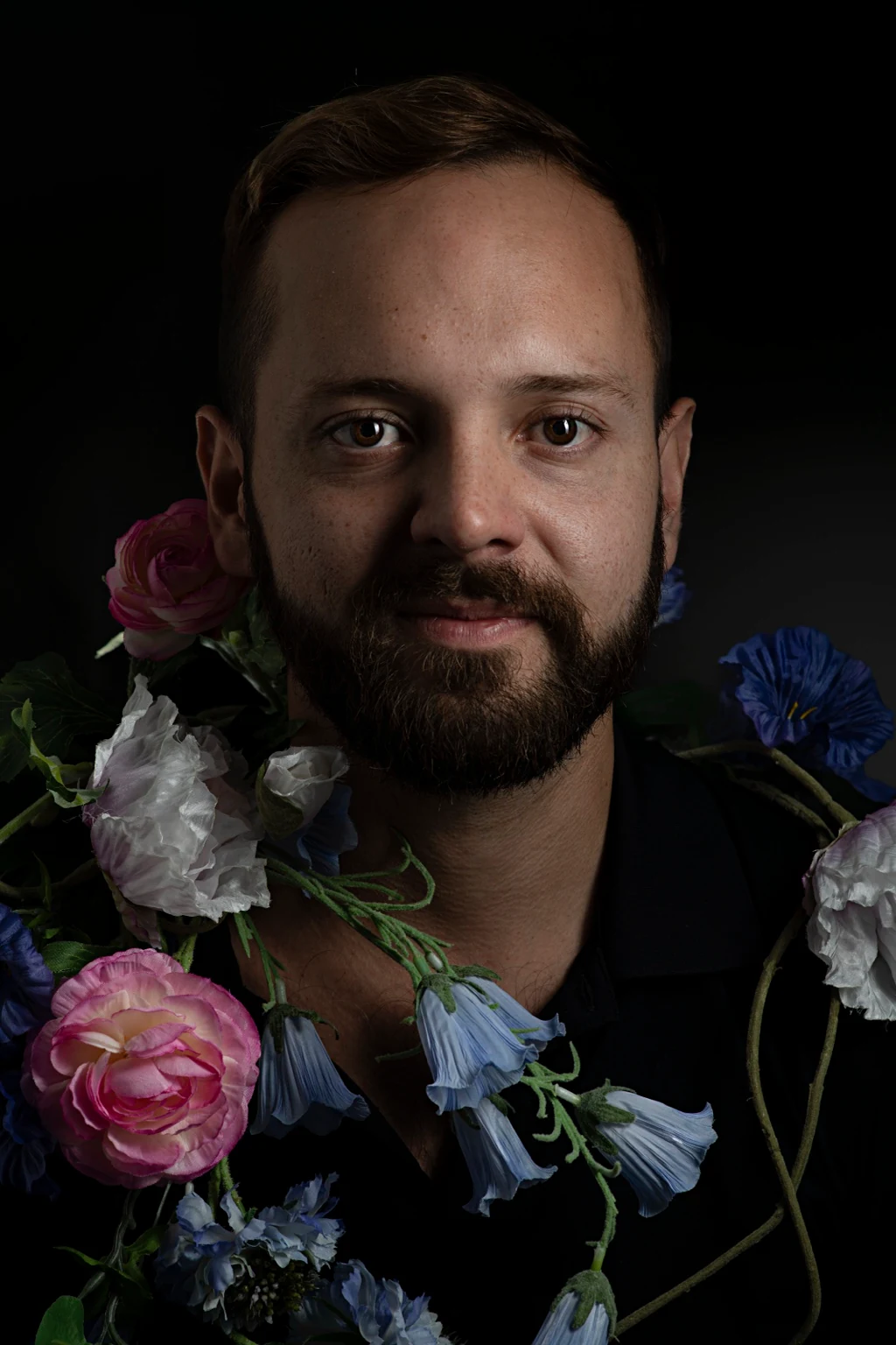 A bearded face surrounded by pink, white and blue flowers.