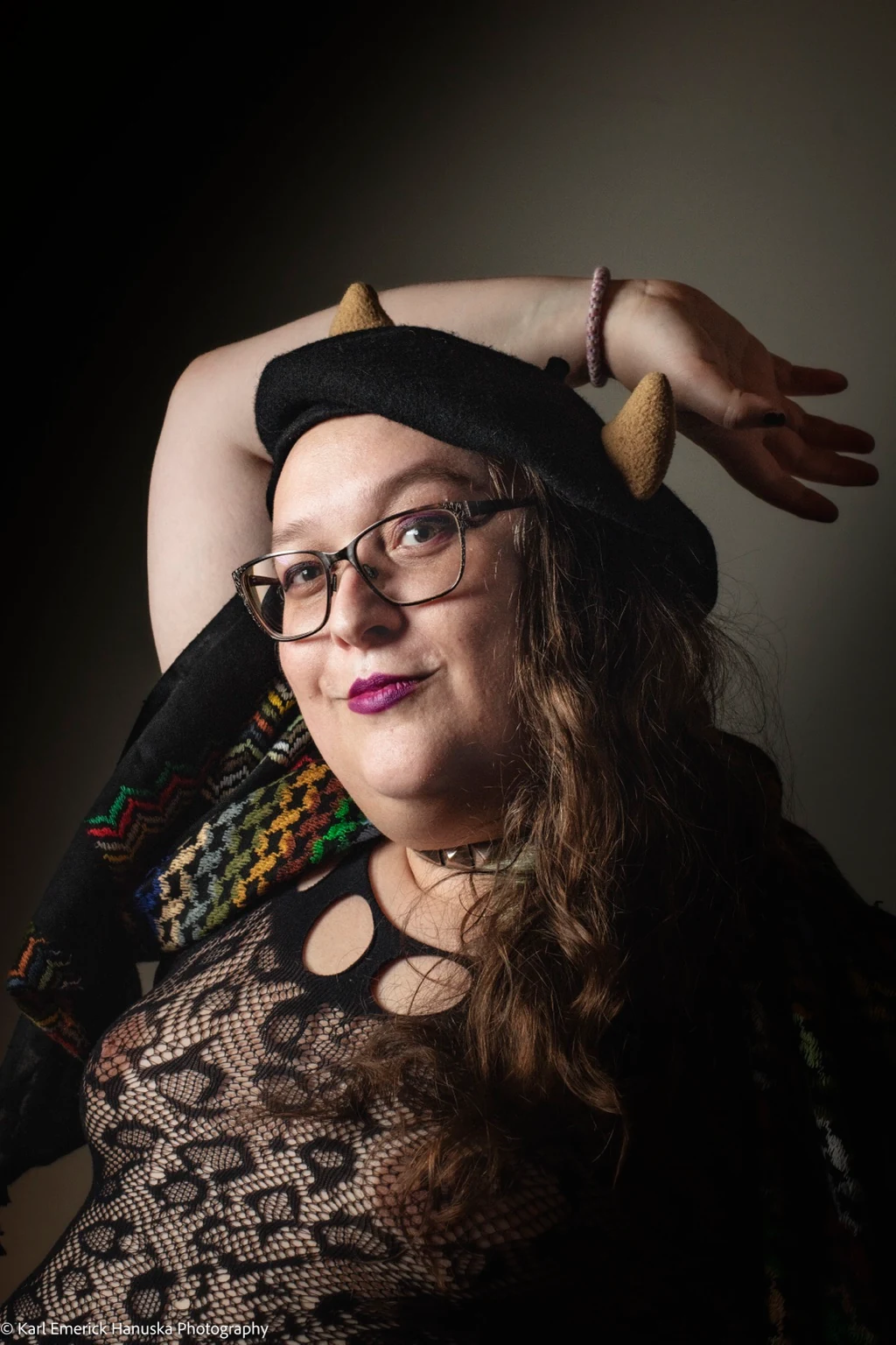 A sitter in glasses, a horned beret and a lace top holds an arm above the head.