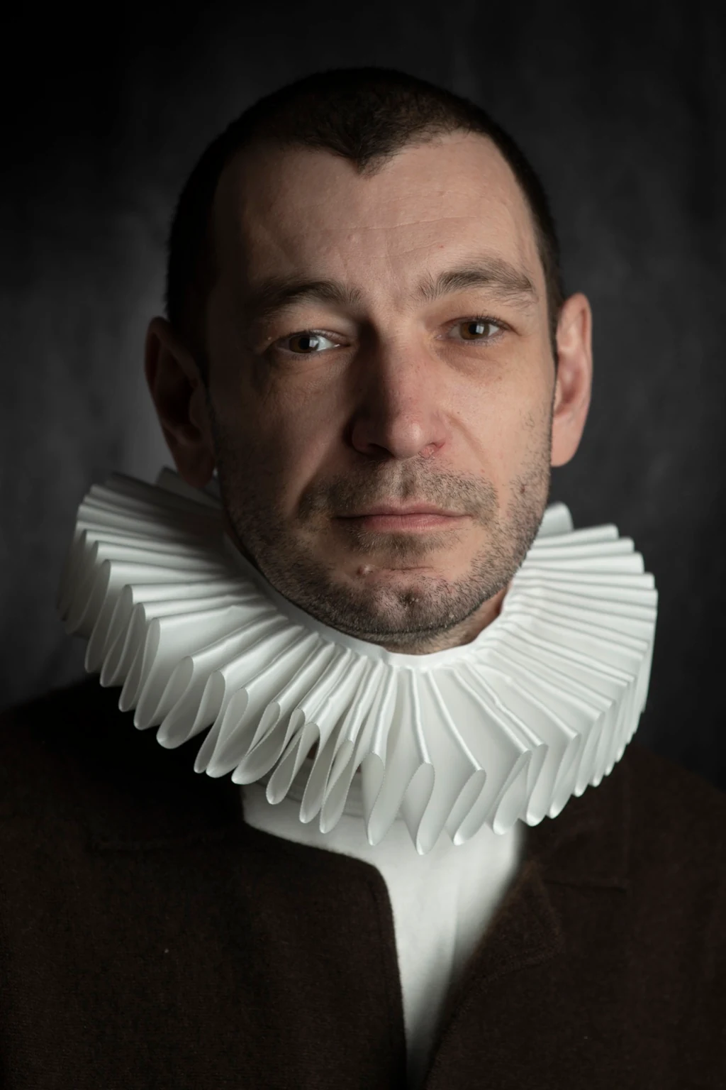 A close portrait of a sitter wearing a sculptural white pleated ruff and a dark jacket.