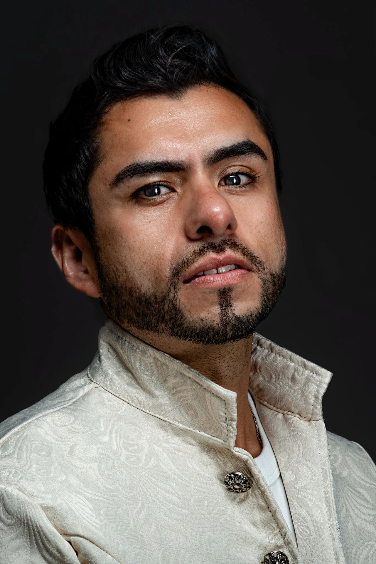 A close portrait of a sitter wearing a textured ivory jacket with a high collar and decorative clasp.