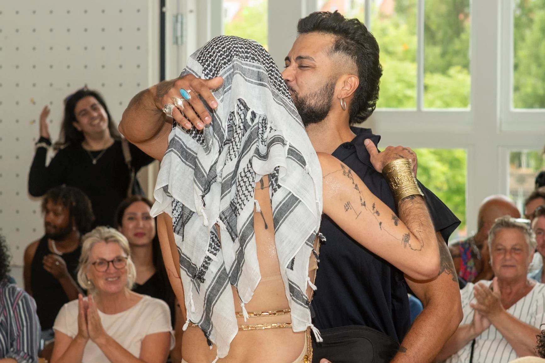 Two people embrace and kiss while the seated audience applauds.