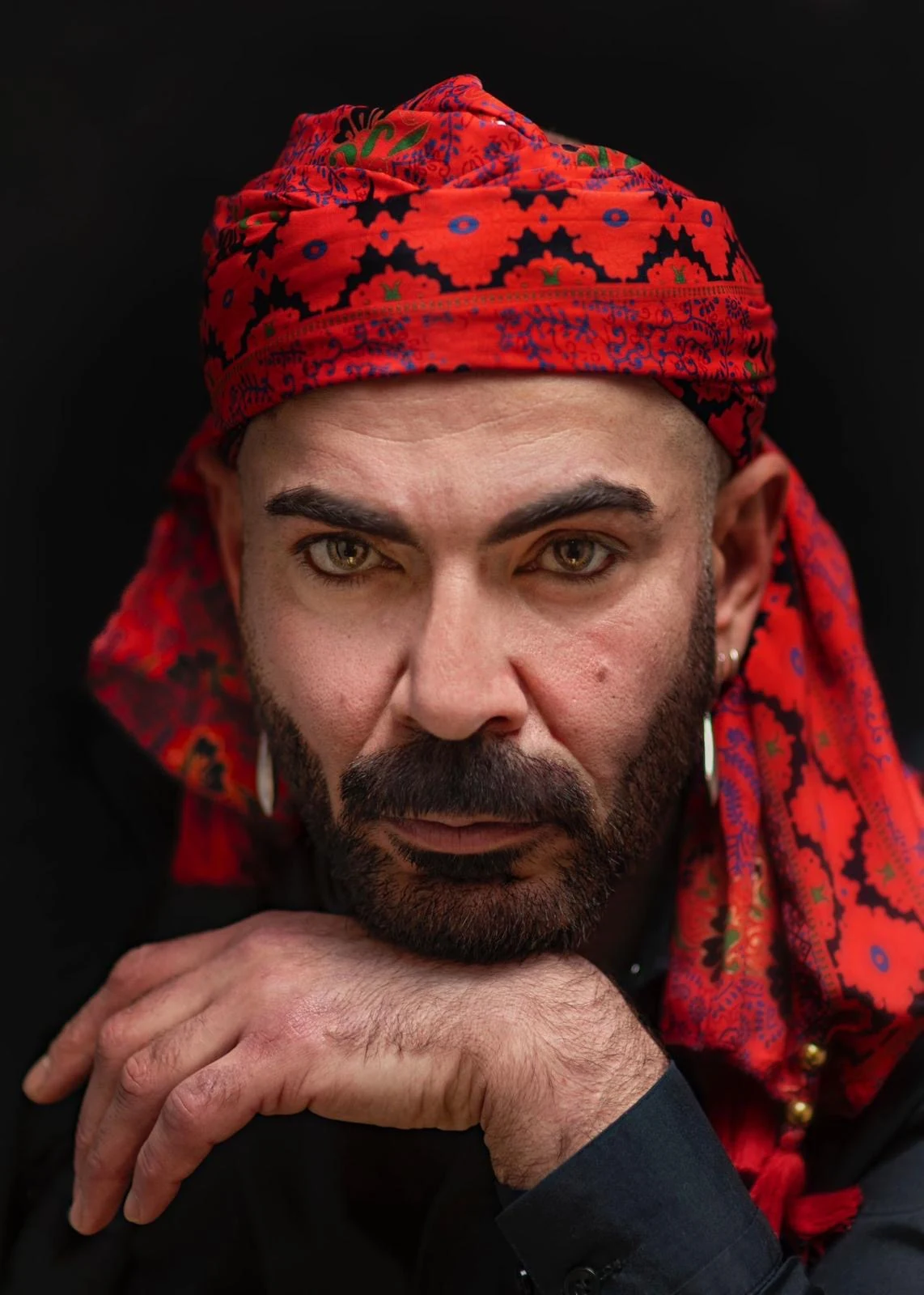 A bearded sitter in a red patterned headwrap rests the chin on one hand.