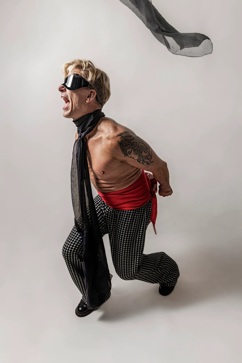 Self-portrait lunging forward with an open mouth, dark goggles and a flying scarf.