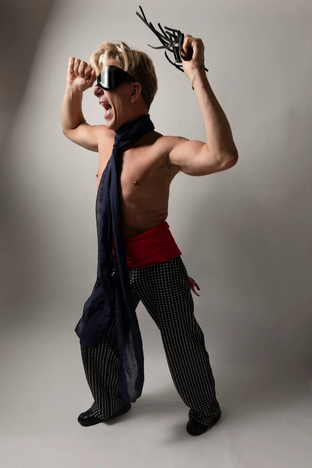 Self-portrait with raised arms, goggles and patterned trousers.